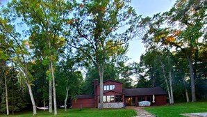 A two-story wooden cabin with a stone foundation, surrounded by a stone pathway and a grassy yard. - Private Beach, Beautiful Lake Home, Fishing, Recreation - Everything You Need! (Crosslake)