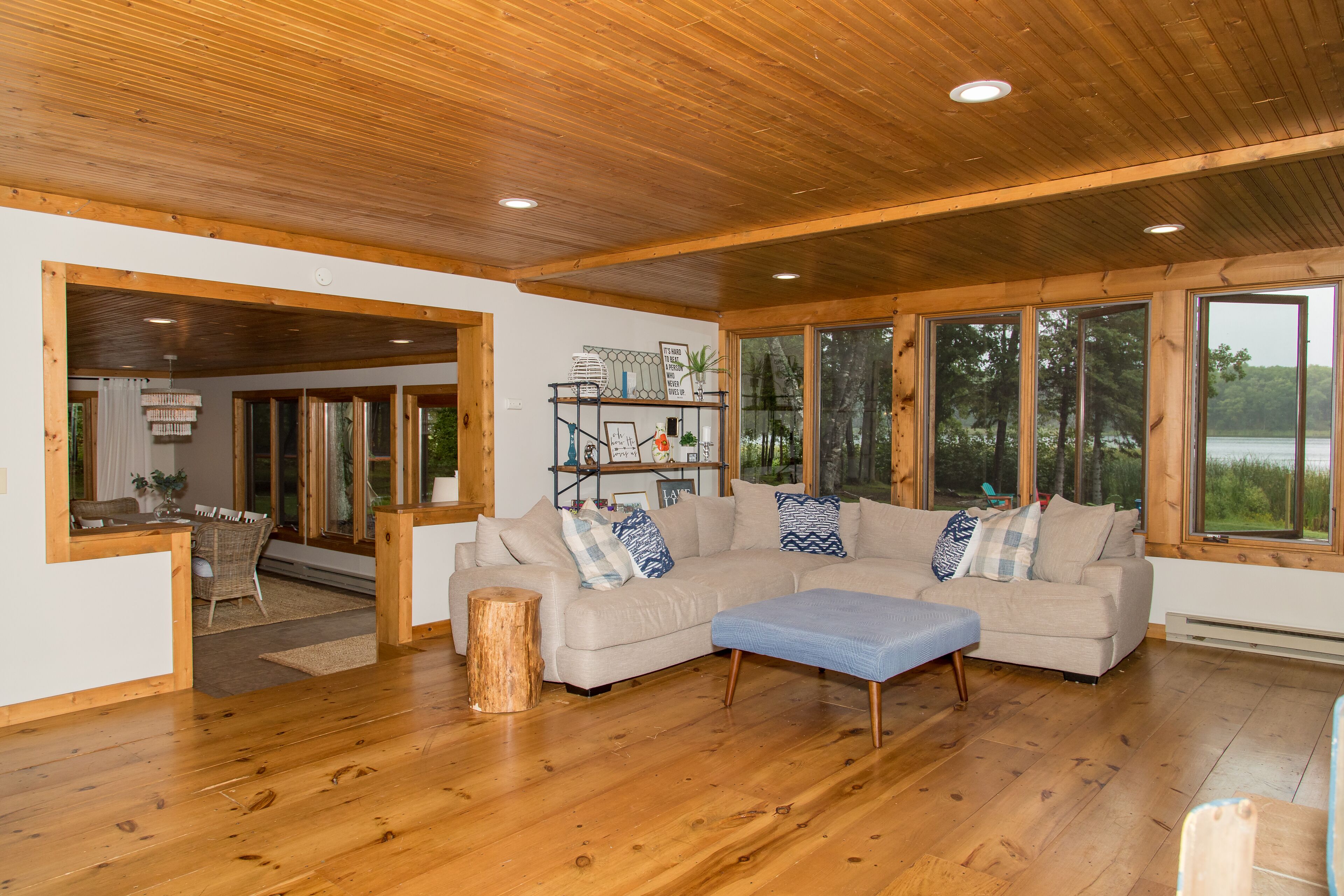 A spacious living room with a wooden ceiling, large windows, a beige sectional sofa, and a wooden floor.