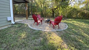 A patio area with two Adirondack chairs and a small table, surrounded by a gravel border and grass.