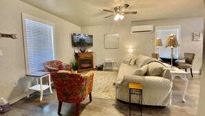 A living room with a fireplace, a ceiling fan, a television, and a dining area with chairs and a table.