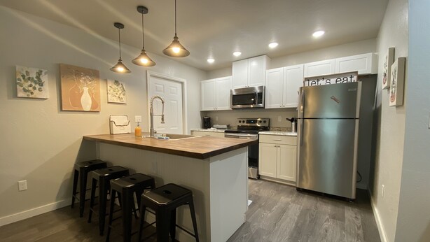 A modern kitchen with a central island, bar stools, stainless steel appliances, and pendant lighting.