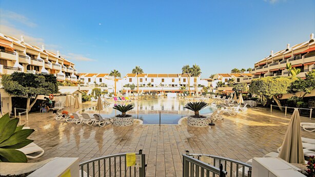 Ein Hotelinnenhof mit einem zentralen Pool, Liegestühlen und Blumentöpfen.