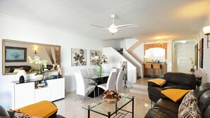 Ein modernes Wohnzimmer mit einem Glastisch, einem schwarzen Ledersofa und einem Essbereich mit weißen Stühlen.