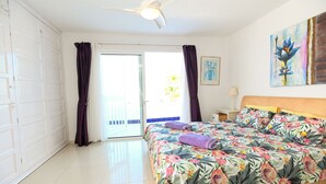 Ein Schlafzimmer mit Bett, Deckenventilator, Nachttisch, Lampe und einem Bild an der Wand.