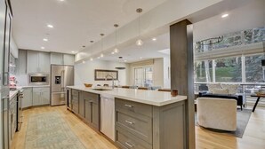 A modern kitchen with a large island, stainless steel appliances, pendant lighting, and a view of the outdoors.