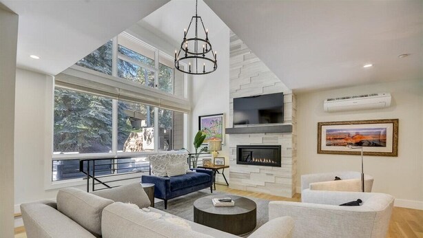 A spacious living room with a high ceiling, large windows, a fireplace, and a modern chandelier.