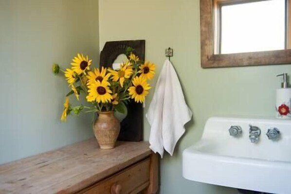 A bathroom with a wooden vanity, a white sink, and a vase of sunflowers. - The Valley House, Unit 2 (Sierraville)