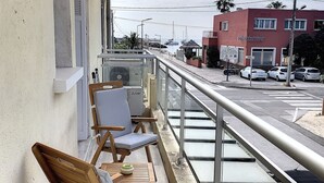 A balcony with wooden chairs and a table, overlooking a street with parked cars and a building with a sign. - Charming apartment sea view (HYERES)