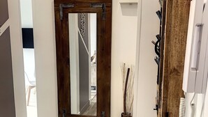 A room with a large mirror on the wall, a wooden door, and a vase with dried plants. - Charming apartment sea view (HYERES)