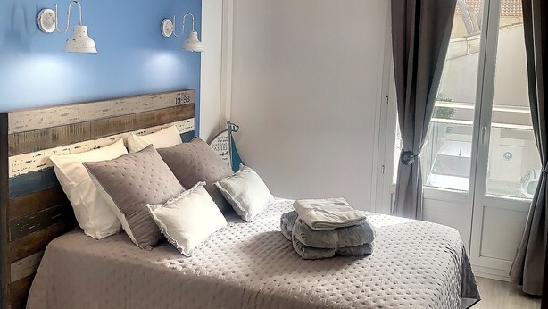 A bedroom with a bed, a hanging light fixture, a window with curtains, and an air conditioning unit. - Charming apartment sea view (HYERES)