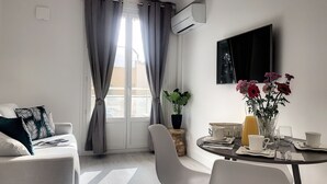 A modern living room with a sofa, dining table, and chairs. There is a potted plant and a vase with flowers on the table. - Charming apartment sea view (HYERES)