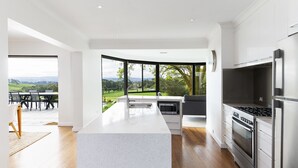 A modern kitchen with a large island, stainless steel appliances, and a view of a green landscape.