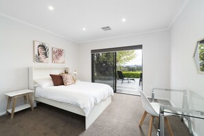 A bedroom with a bed, a glass table, and a view of the outdoors. - Farm Stay at The Farm Barn (Hahndorf)
