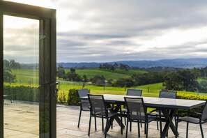 A patio with a table and chairs, overlooking a green landscape with hills. - Farm Stay at The Farm Barn (Hahndorf)