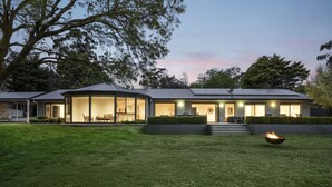 A modern house with a large glass facade, a well-maintained lawn, and a fire pit.