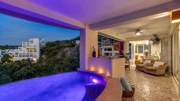 Uma área moderna de piscina interna com vista para um horizonte urbano ao entardecer.