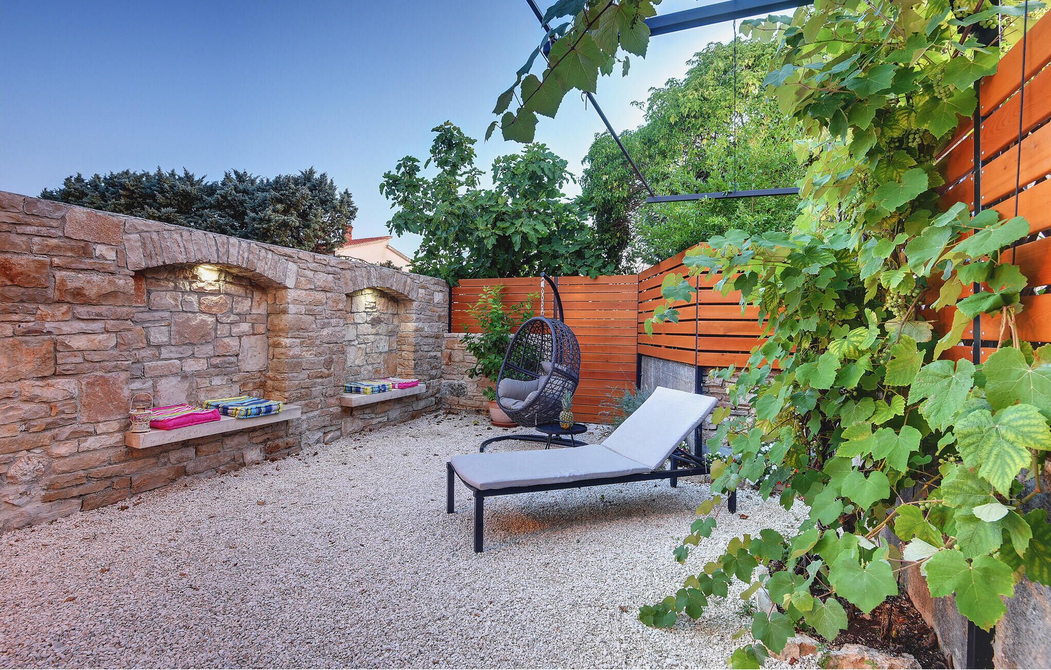 Un espace patio agrémenté d’un mur en pierre, d’une chaise suspendue, d’un fauteuil et d’une clôture en bois.