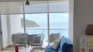 Ein modernes Wohnzimmer mit großem Fenster zum Meer, einem Essbereich mit Tisch und Stühlen sowie Blick auf den Ozean.