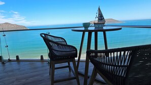 Ein Balkon mit Korbstühlen und einem Tisch, mit Blick auf ein klares, blaues Meer und die Ferne.