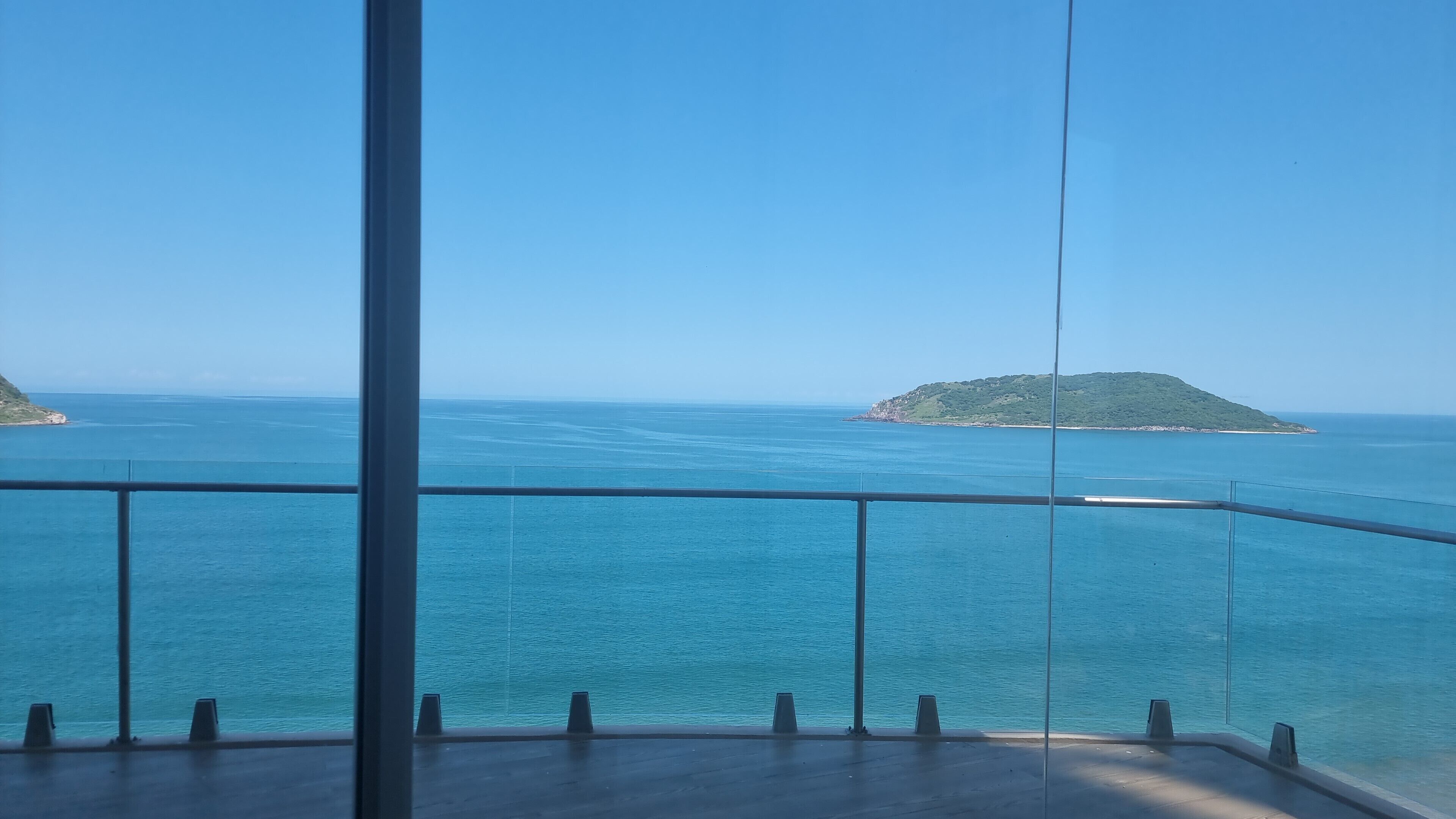 A balcony with a clear view of the sea and a small island.