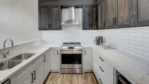 Une cuisine moderne dotée d’appareils électroménagers en acier inoxydable, de carreaux de céramique blancs rectangulaires et de meubles de cuisine en bois foncé.