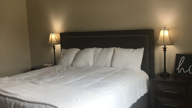 Een slaapkamer met een groot bed, twee bedlampen, een plafondventilator en een nachtkastje met een ingelijste foto.