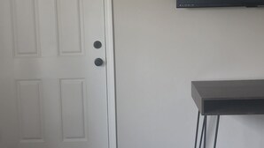 Een kamer met een witte deur, een zwarte televisie aan de muur en een klein zwart tafeltje met metalen poten.
