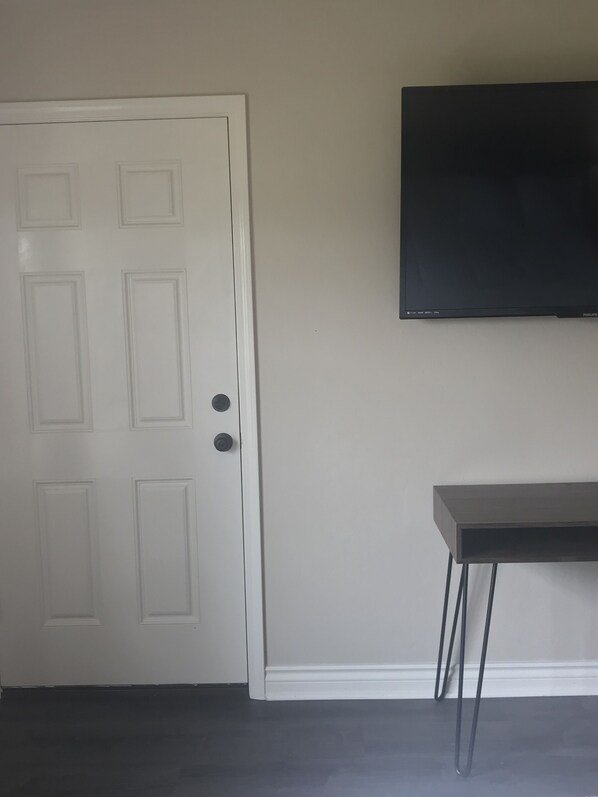 A room with a white door, a black television mounted on the wall, and a small black table with metal legs.