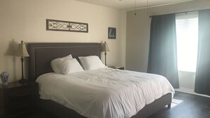 Een net opgemaakt bed met witte lakens, een donker hoofdbord en twee bedlampjes.