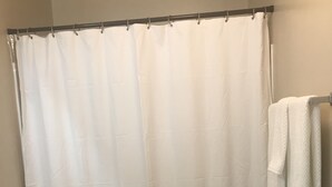 Een badkamer met een witte douchegordijn met een zigzagpatroon, een wit toilet en een witte handdoekhouder met een handdoek.