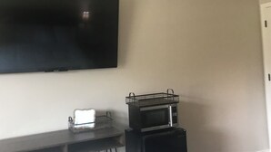 Een kamer met een wandgemonteerde flatscreen-tv, een magnetron op een standaard en een klein tafeltje met een mand en een doos.
