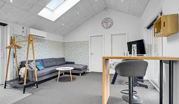 Un salon moderne avec un canapé d’angle gris, une table basse ronde, un meuble TV en bois et un petit tabouret de bar.