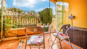 Een balkon met twee stoelen, een tafeltje en uitzicht op gebouwen en groen.