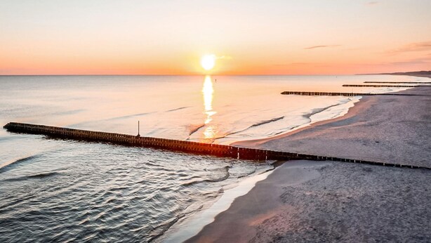 A beach with a long pier extending into calm waters, reflecting the sunset. - Stunning home in Nowecin with kitchen (Nowecin)