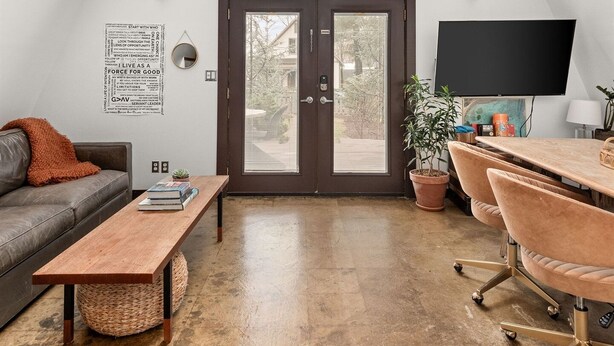 Ein geräumiges Loft mit hoher Decke, einem großen Fenster, einem Holzespeisetisch, einer Couch und einem Fernseher.