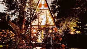 Eine dreieckige Glasstruktur mit Lichtquelle im Inneren, umgeben von Bäumen und einem Weg.