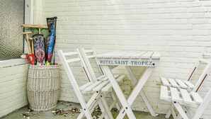 Un panier en osier blanc contenant du matériel de nettoyage, des chaises pliantes blanches et une pancarte indiquant « HÔTEL SAINT-TROPEZ ».
