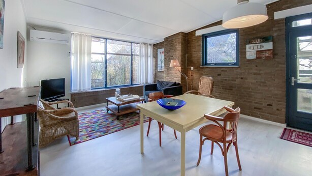 Un salon moderne avec un coin repas, de grandes fenêtres et un mur en briques.
