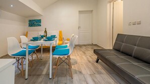 A dining area with a table set for four, four white chairs with blue cushions, a black sofa, and a white door in the background. - 1 bedroom beautiful apartment in Vir (Vir)