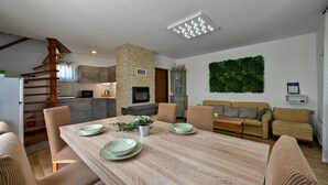 A modern kitchen with a stone wall, a dining area with a wooden table and chairs, and a living area with a sofa and a green wall decoration. - Cozy home in Biskupec Zelinski with sauna (Biskupec Zelinski)