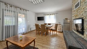 A modern living room with a stone wall, a wooden dining table, and a TV mounted on the wall. - Cozy home in Biskupec Zelinski with sauna (Biskupec Zelinski)