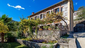 Il s’agit d’un bâtiment traditionnel en pierre, doté d’un jardin à l’avant, comprenant un mur en pierre, une pergola couverte de plantes grimpantes et une variété de plantes.