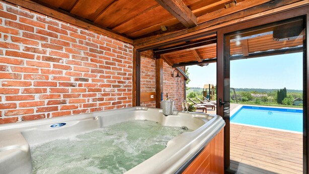 A hot tub with a brick wall backdrop, a wooden deck, and a view of a swimming pool. - Amazing home in Nova Diklenica with sauna (Nova Diklenica)