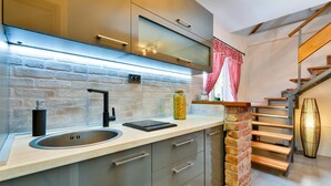 A modern kitchen with a brick accent wall, stainless steel appliances, and a wooden staircase. - Amazing home in Nova Diklenica with sauna (Nova Diklenica)