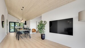 Ein modernes Interieur mit Essbereich, einer großen Pflanze im Topf und einem an der Wand befestigten Flachbildfernseher.