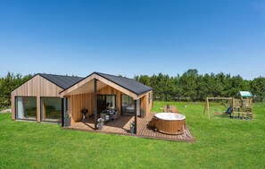 A modern wooden cabin with a large deck, a hot tub, and a children's play structure in a grassy area. - 3 bedroom stunning home in Jerup (Jerup)