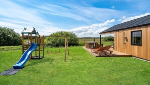 Eine Holzhütte mit Sauna, einer Holzspielanlage mit Rutsche und einer Terrasse mit Liegestühlen.