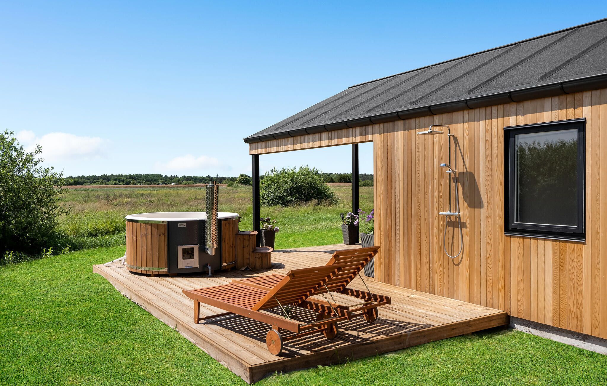 Eine Holzhütte mit Whirlpool, einer Holzterrasse und einer Dusche.