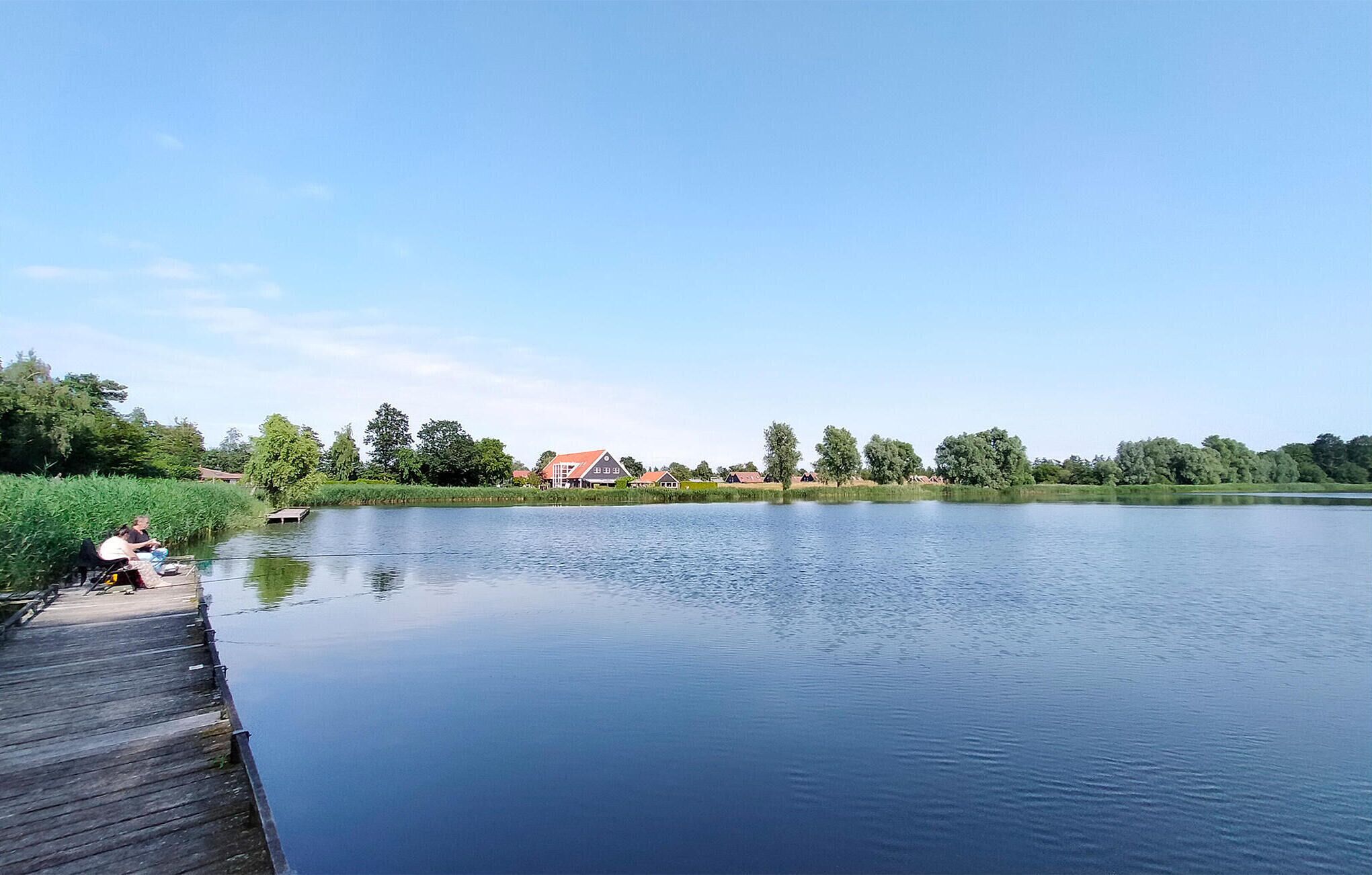 Ein ruhiger See mit einer hölzernen Mole und einer Häuserreihe im Hintergrund.