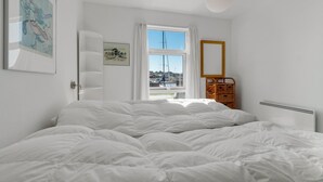 A bedroom with a large bed, a window with a view of a marina, a wicker basket, and a framed picture on the wall. - Beach front home in Hasle (Hasle)